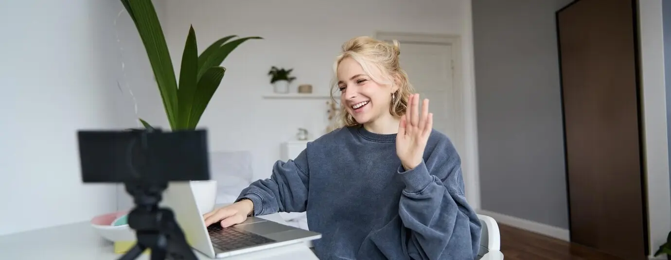 Porträt einer jungen Social-Media-Content-Creatorin, die in einem Raum mit Laptop und Digitalkamera sitzt.